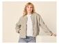 Femme en blouson aviateur gris clair, t-shirt blanc et jean, posant sur fond clair.