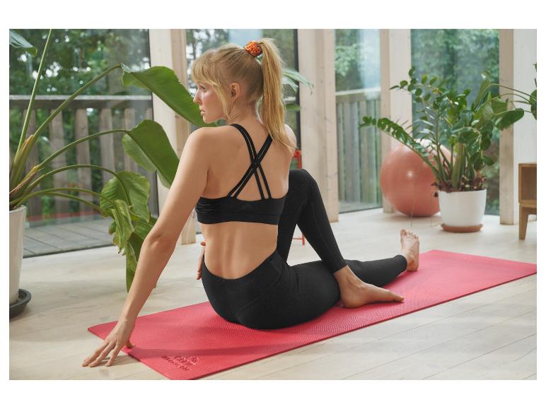 Femme en leggings et brassière de sport noirs, faisant du yoga sur un tapis rouge.