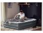 Un jeune homme assis sur un lit gonflable LIVARNO® Premium avec un ordinateur portable et un casque.