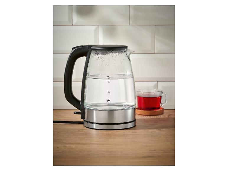 Bouilloire en verre avec de l'eau et une tasse de thé rouge sur une table en bois.