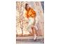 Une femme portant un pull orange, une jupe beige et des baskets blanches.