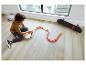Un garçon joue avec une piste de course Hot Wheels et un skateboard.