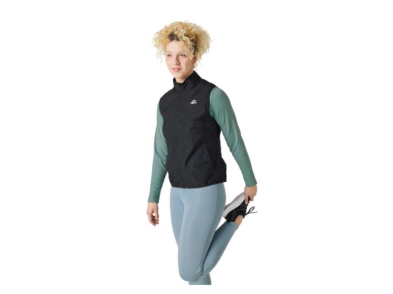 Femme aux cheveux bouclés s'étirant, portant un gilet de sport Crivit et un legging bleu.