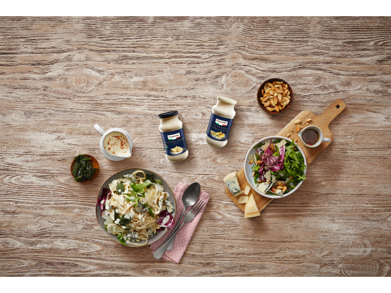 Sauces pâtes et salades avec fromage, noix et herbes sur bois clair.