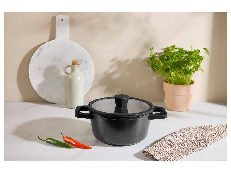 Marmite noire avec couvercle, piments, planche à découper et herbes en cuisine