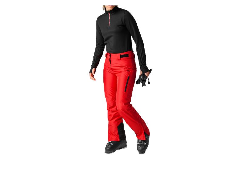 Femme en pantalon de ski rouge et haut noir, avec des chaussures de ski.