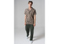 Un homme portant une chemise beige à motif noir et un pantalon vert.