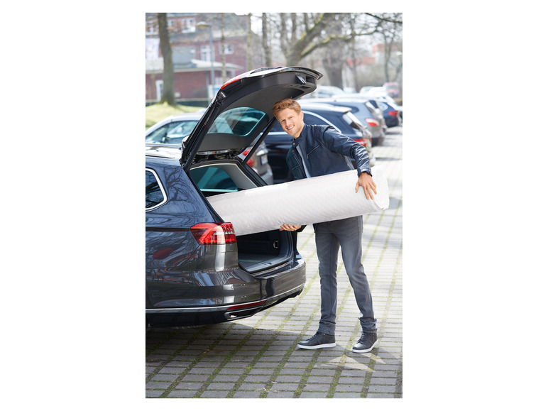 Un homme met un matelas dans le coffre d'une voiture.