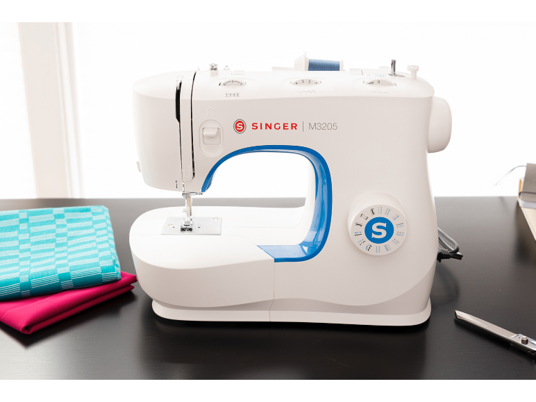 Machine à coudre blanche avec des accents bleus, du tissu et des ciseaux sur une table sombre.