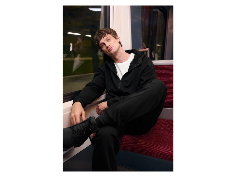 Un homme porte un sweat-shirt à capuche noir et un pantalon noir dans un train.