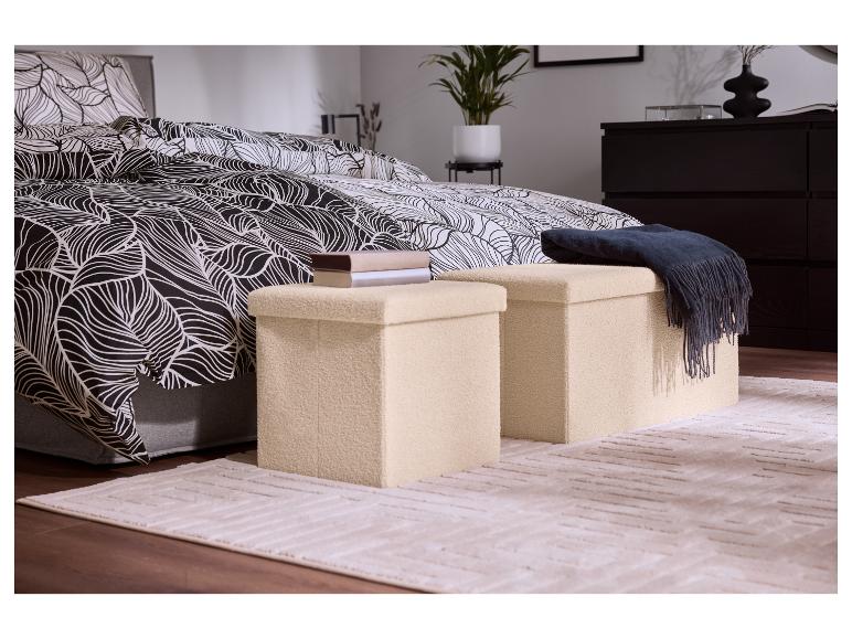 Chambre à coucher avec housse de couette à motif de feuilles noires et blanches, deux poufs de rangement beiges et un tapis.