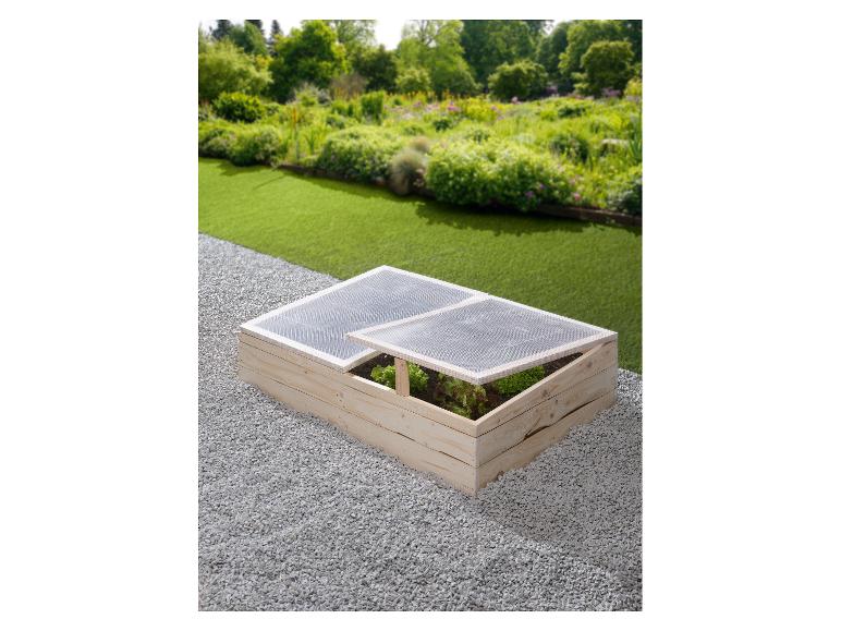 Châssis froid en bois avec couvercle transparent et légumes dans un jardin.