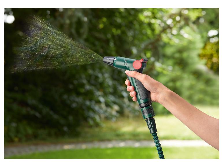Main tenant un pistolet d'arrosage vert projetant de l'eau dans un jardin.