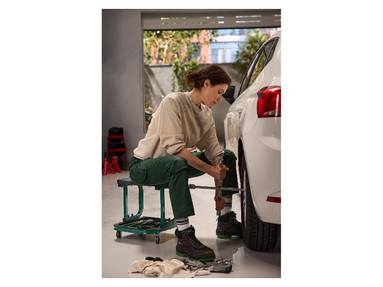 Une femme assise sur un tabouret d'atelier à roulettes PARKSIDE pendant qu'elle change un pneu.