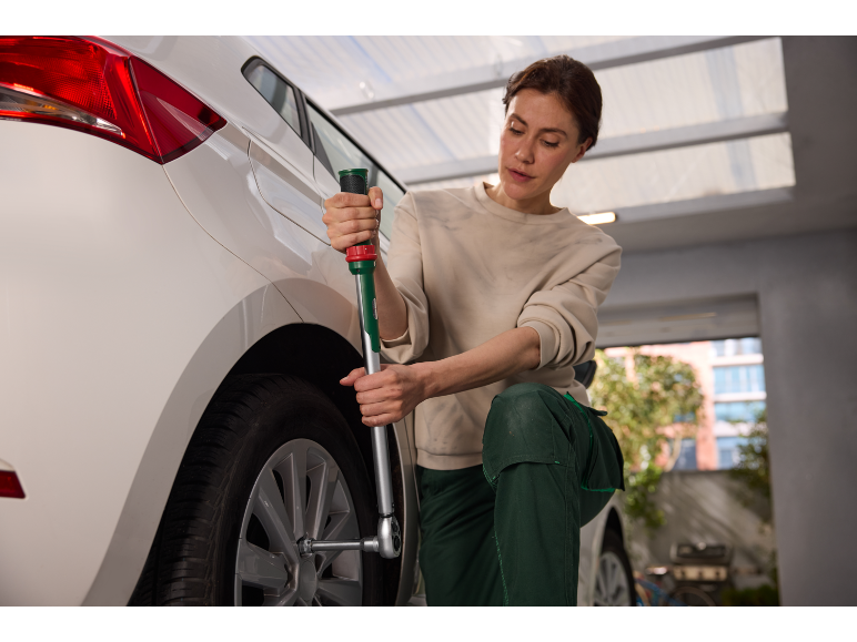 Femme changeant un pneu de voiture avec une clé en croix dans un garage.