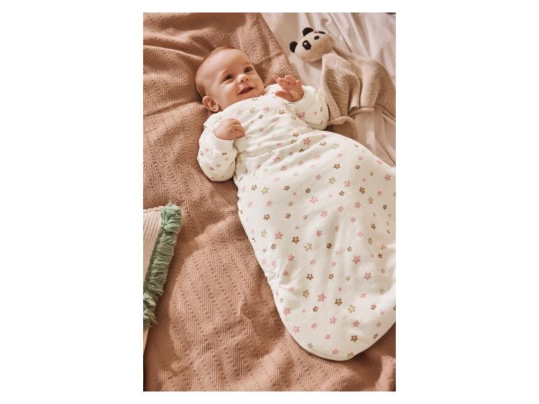 Bébé dans gigoteuse étoilée, allongé sur une couverture avec une peluche panda.