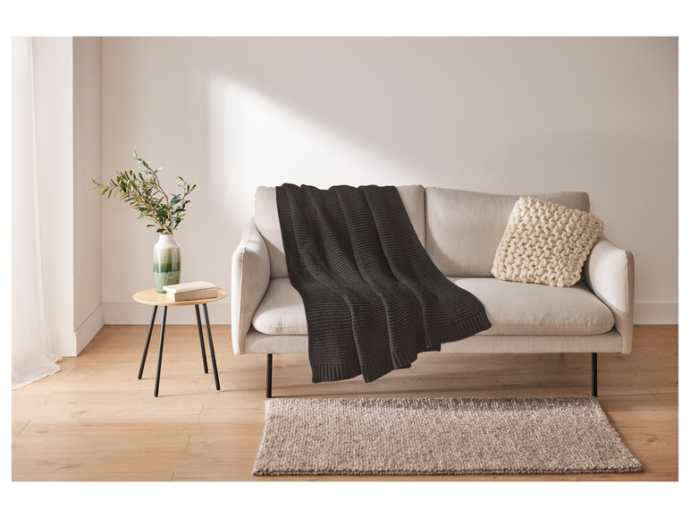 Une couverture en tricot gris foncé sur un canapé clair.