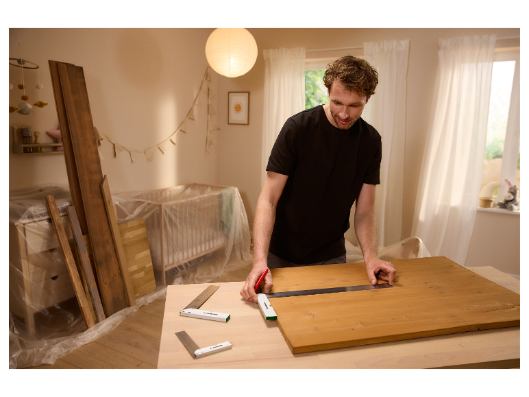 Un homme utilise des équerres et un mètre Parkside pour mesurer une planche de bois.