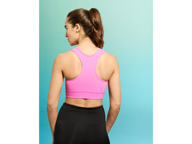 Une femme porte un soutien-gorge de sport rose et un legging noir.