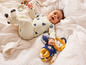 Un bébé portant un t-shirt blanc avec des bateaux bleus, tenant un lion en peluche jaune.
