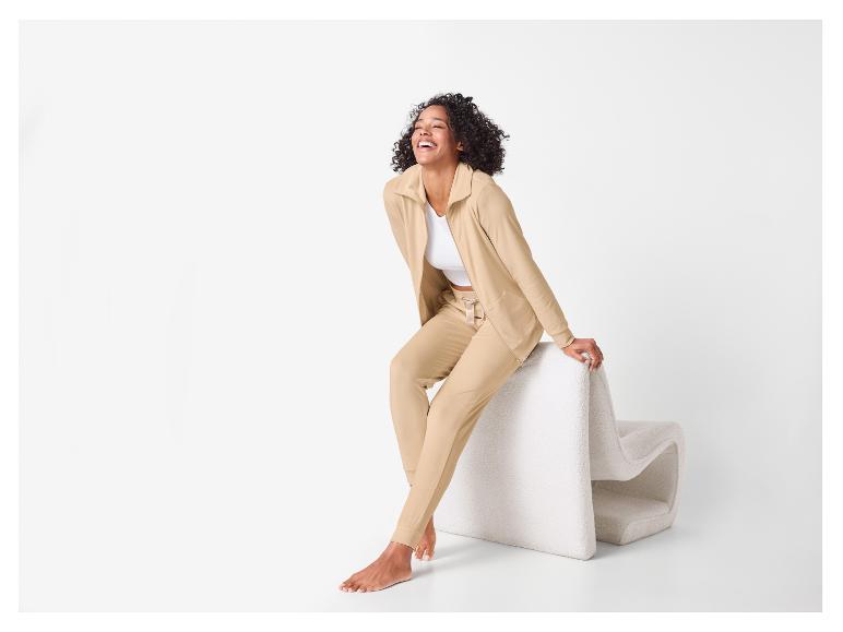Femme en survêtement beige et haut blanc assise, souriante
