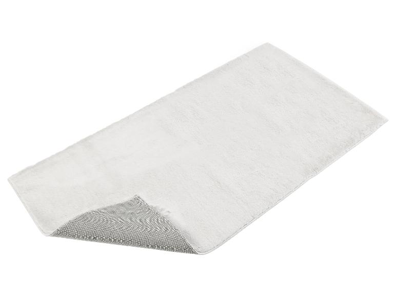 Un tapis blanc et pelucheux avec un dessous gris.