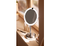 Miroir de maquillage rond avec éclairage LED sur un rebord de fenêtre ensoleillé.