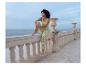 Femme en débardeur vert et pantalon imprimé assise sur un balcon avec vue sur la mer.