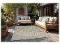Terrasse avec mobilier de jardin en bois, coussins clairs et tapis à motifs.
