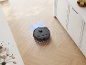Robot aspirateur noir aspirant un sol en bois clair dans une cuisine.