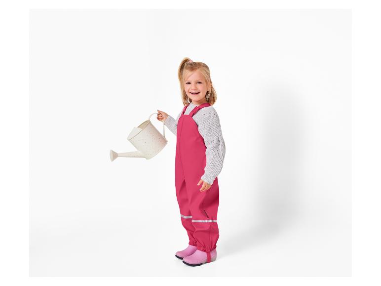 Une fille avec un pantalon de pluie rose tenant un arrosoir blanc.