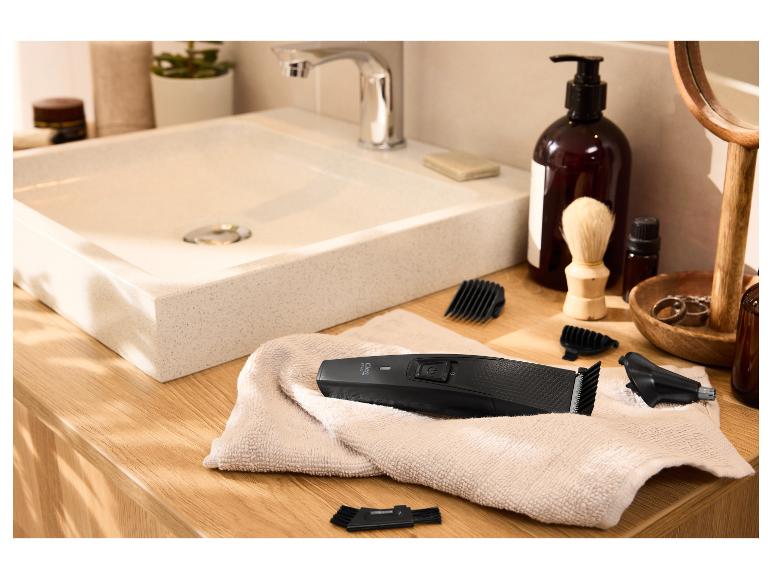 Tondeuse à cheveux et accessoires sur une serviette dans une salle de bain avec lavabo.