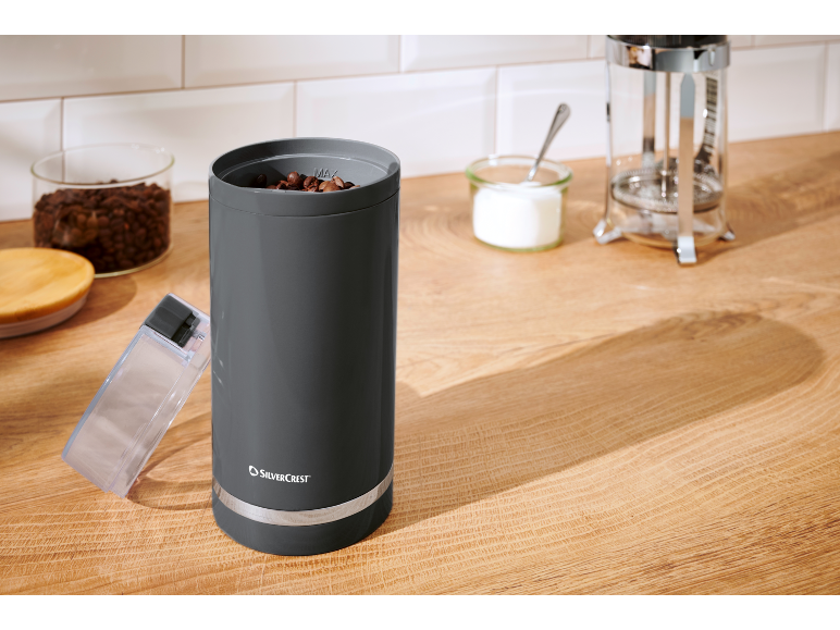 Moulin à café avec grains, sucre et cafetière à piston sur un comptoir en bois.