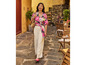 Une femme en blouse à fleurs rose et pantalon blanc marche le long d'une terrasse.