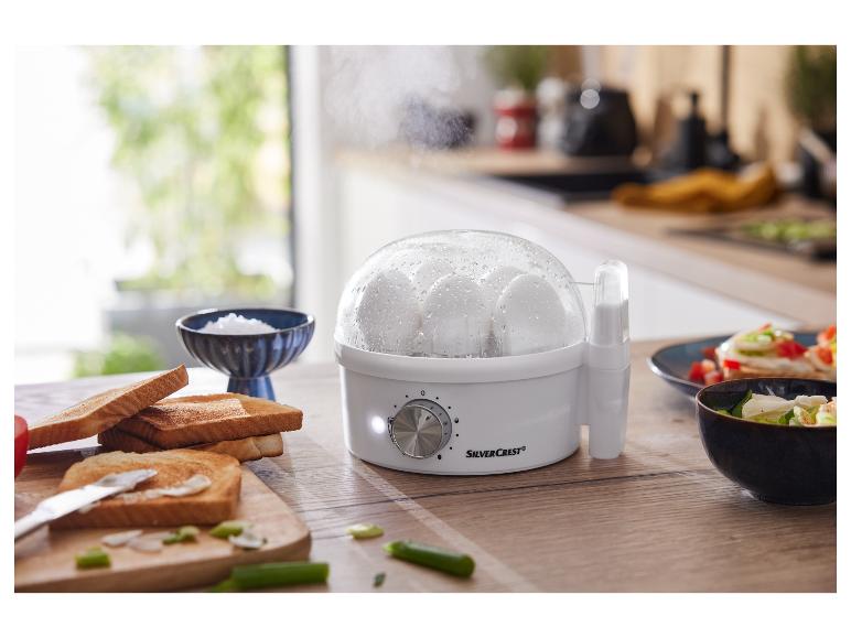 Un cuiseur à œufs blanc SilverCrest avec des œufs cuits, des toasts et une salade.