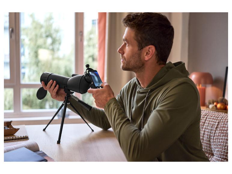 Un homme utilise un télescope noir avec un smartphone monté sur un trépied.