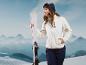 Une femme portant un sweat en fourrure blanche et des lunettes de ski Crivit tient des skis blancs dans les montagnes.