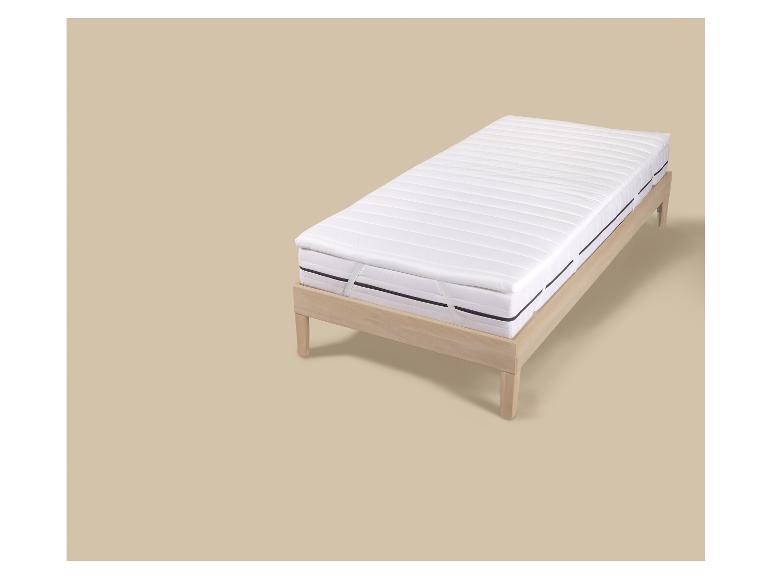 Lit simple en bois clair avec matelas blanc et surmatelas.