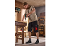 Homme en short de travail noir et t-shirt beige utilisant une perceuse sur un établi.