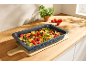 Plat de cuisson avec gratin de légumes et fromage sur une planche à découper en bois.