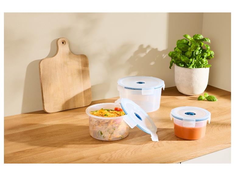 Trois récipients alimentaires transparents avec de la nourriture et une planche à découper sur un comptoir de cuisine.
