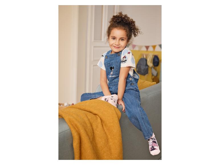 Fille en salopette en jean avec motif Minnie Mouse et t-shirt blanc, assise sur un canapé.