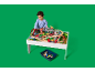Un jeune enfant joue avec un circuit de train en bois sur une table blanche.