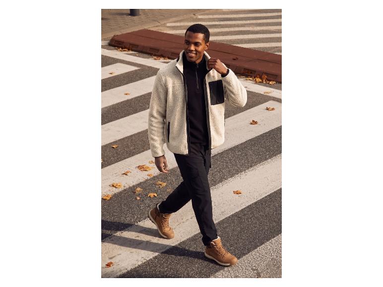 Homme en veste polaire beige, sweat-shirt noir et pantalon noir traversant un passage piéton.