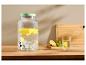 Distributeur de boissons en verre avec citrons et menthe, verre d'eau avec citron sur une table en bois.