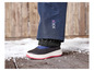 Une paire de bottes d'hiver noires avec une semelle rouge, sur un sol en bois avec de la neige.
