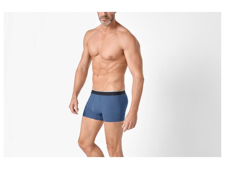 Homme torse nu en boxers bleus, posant sur fond blanc.