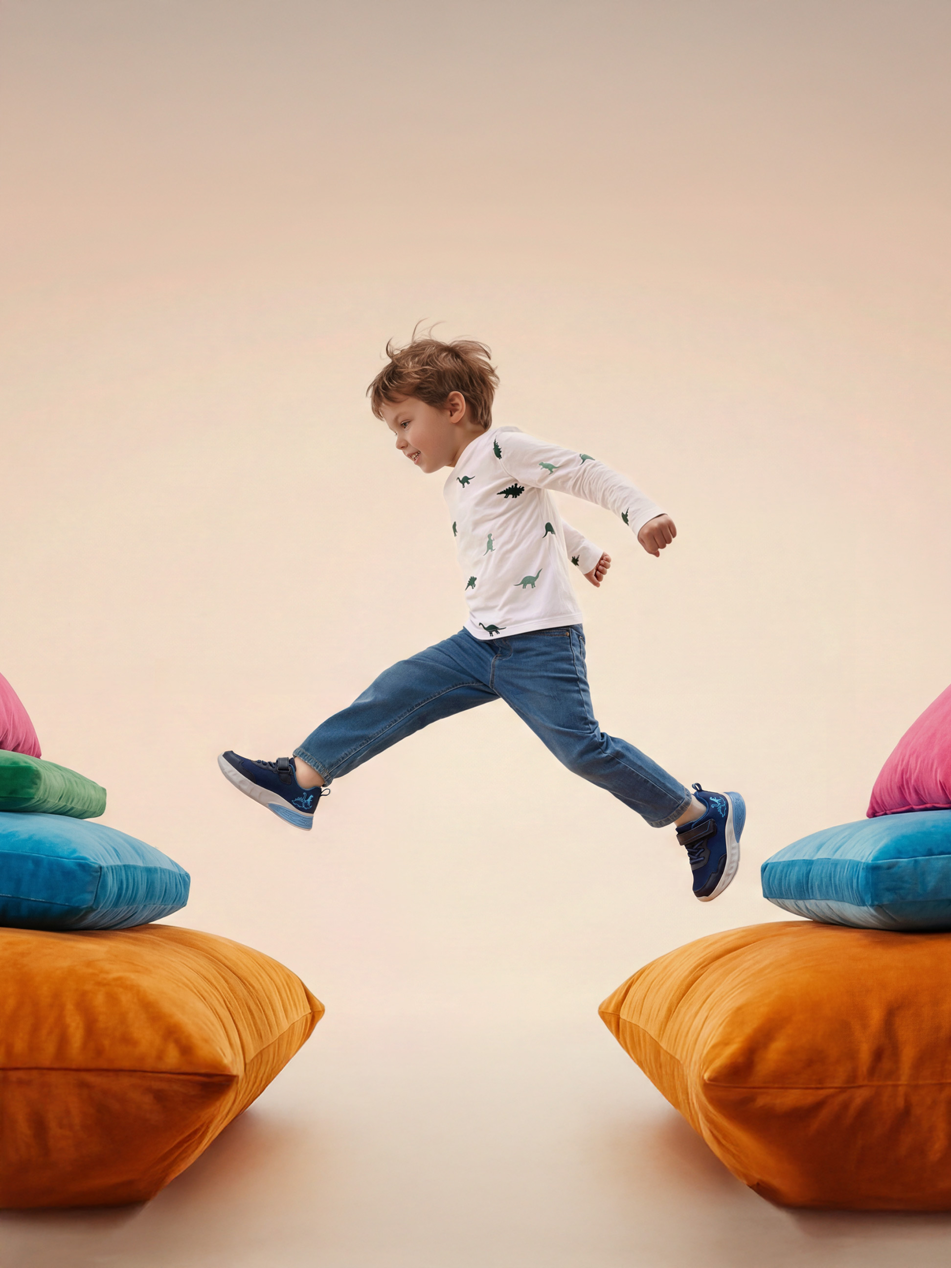 Enfant sautant entre des coussins colorés, portant un t-shirt dinosaure et un jean.