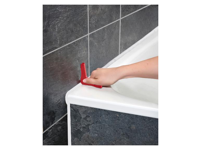 Une main utilisant un outil rouge pour appliquer du mastic autour d'une baignoire blanche.