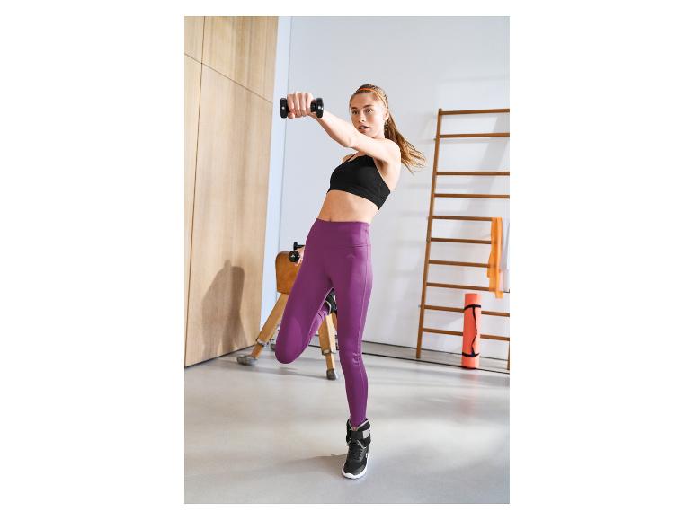 Femme en brassière de sport noire et legging violet faisant de l'exercice avec des haltères